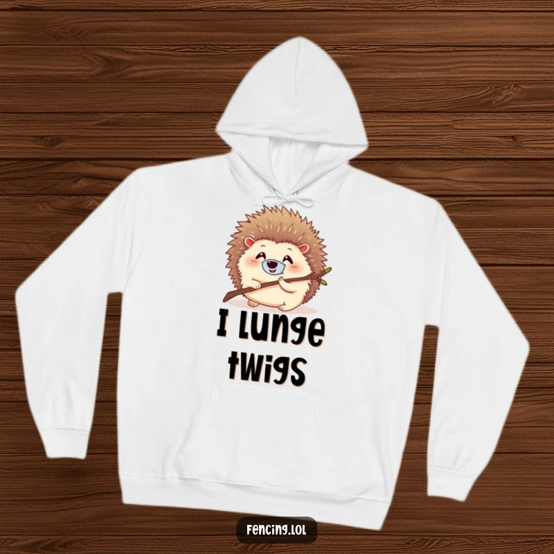 Funny hoodie showcasing a round, smiling hedgehog wearing a tiny mask, lunging with a twig, bringing warmth and humor.